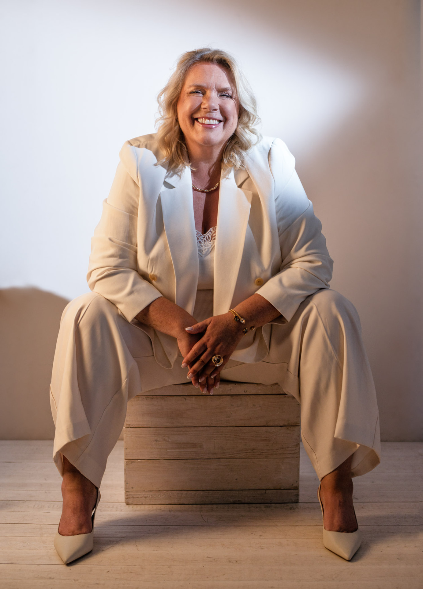 Camilla Ma Ra seated, smiling in a cream suit