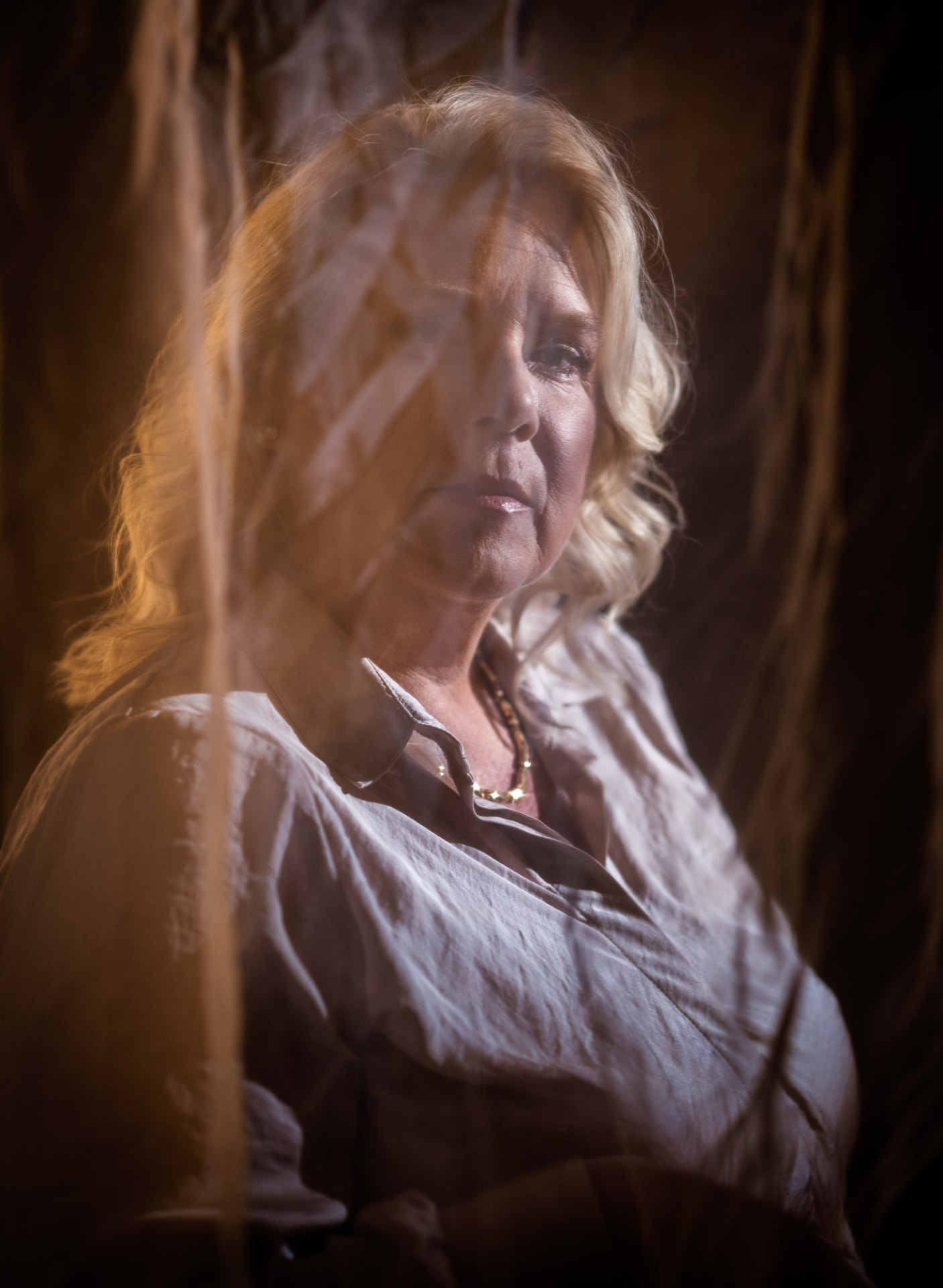 Camilla Ma Ra looking through a sheer curtain in warm light